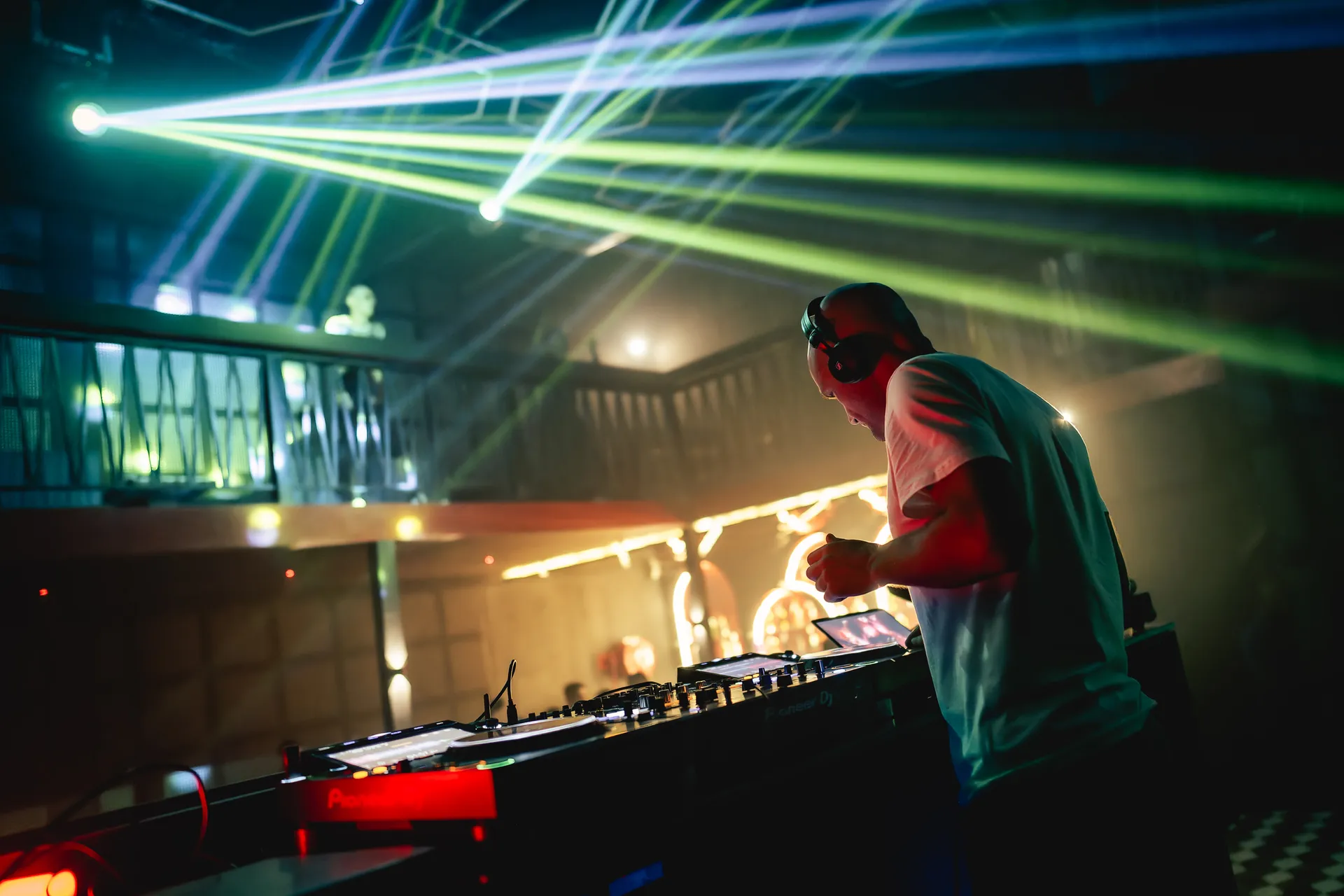 GANGSTANTIN performing at a DJ booth under green stage beams.